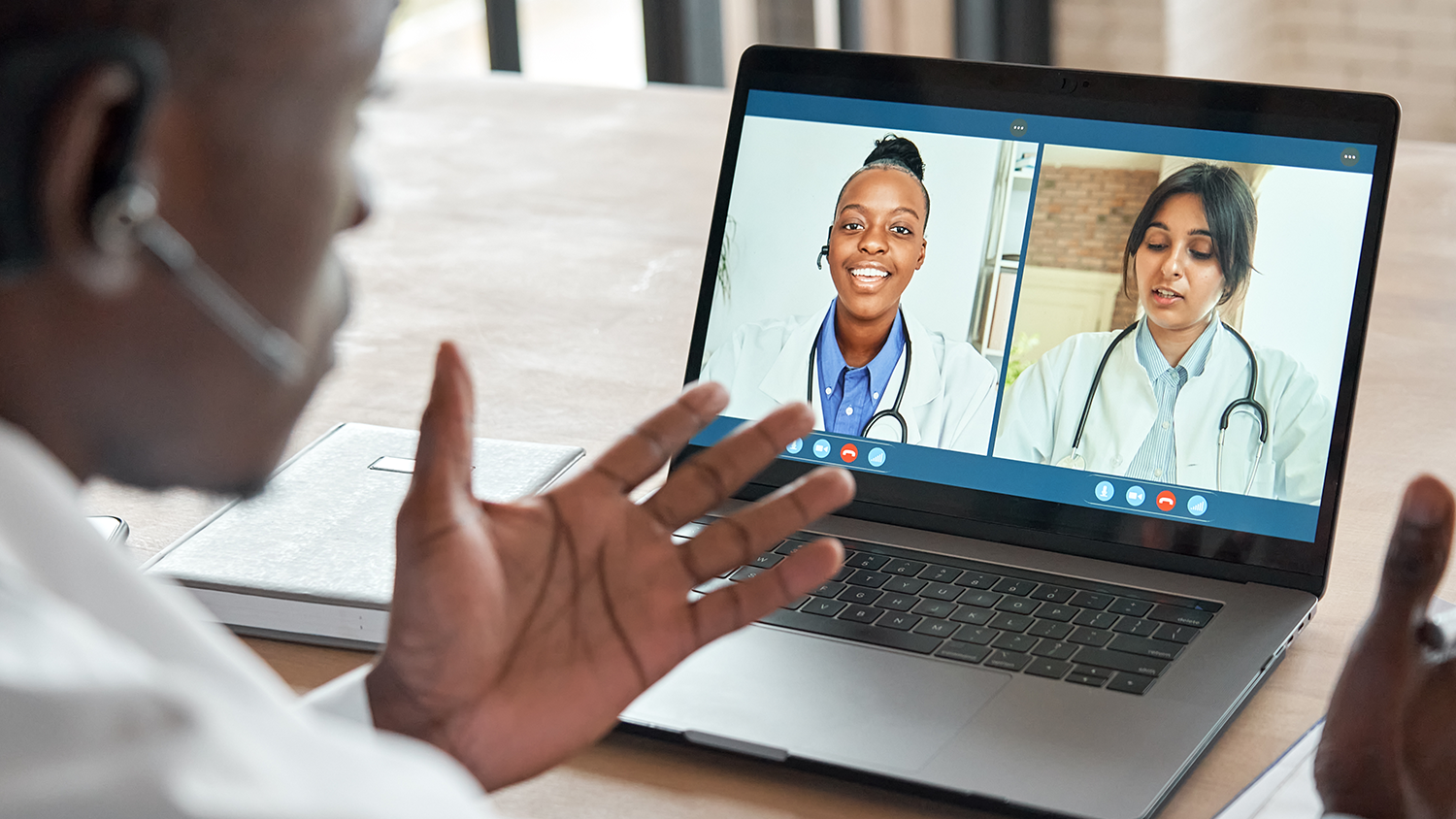 person with headset speaking to two healthcare professionals on a computer